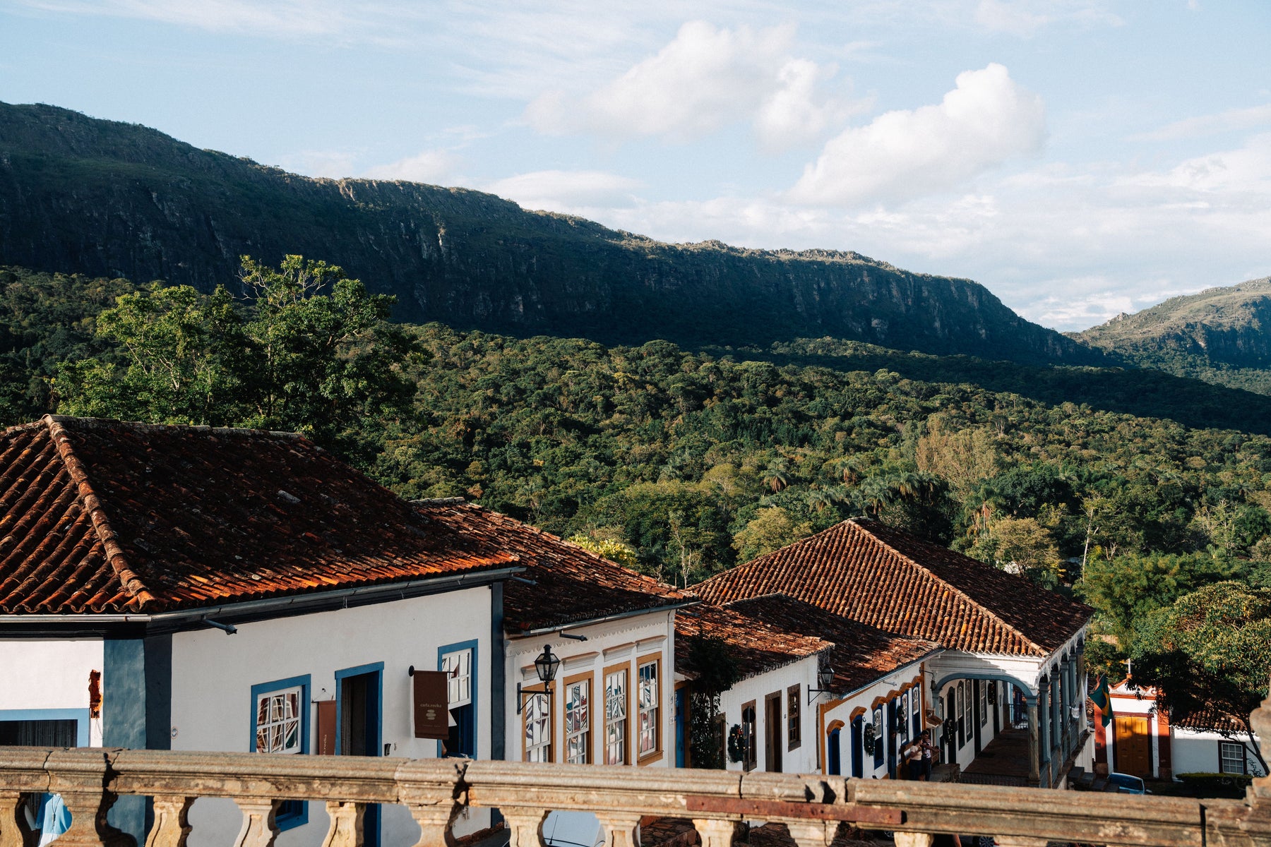Traditional buildings with red tiled roofs beneath forested cliffs