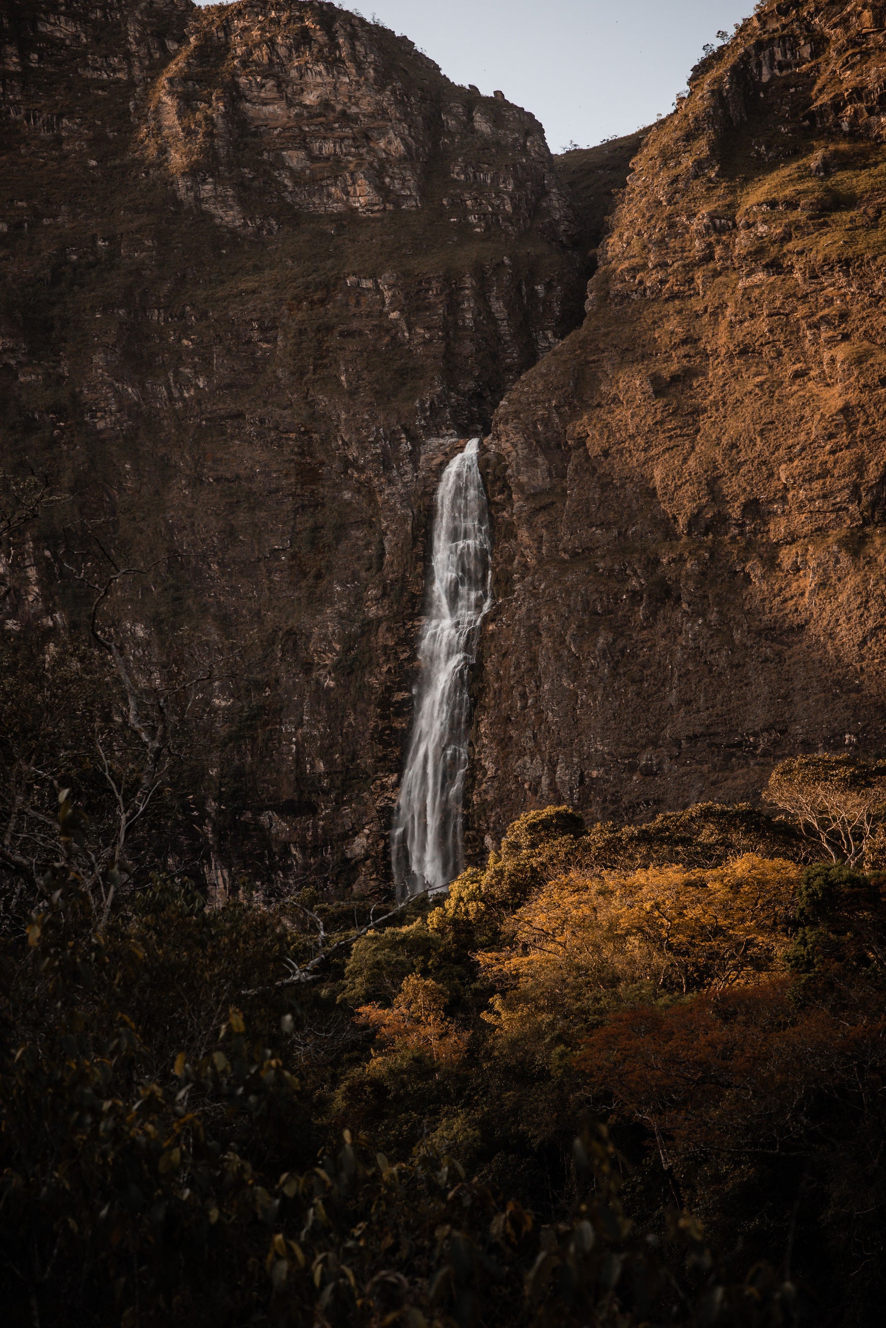 A slender waterfall framed by rugged cliffs and trees