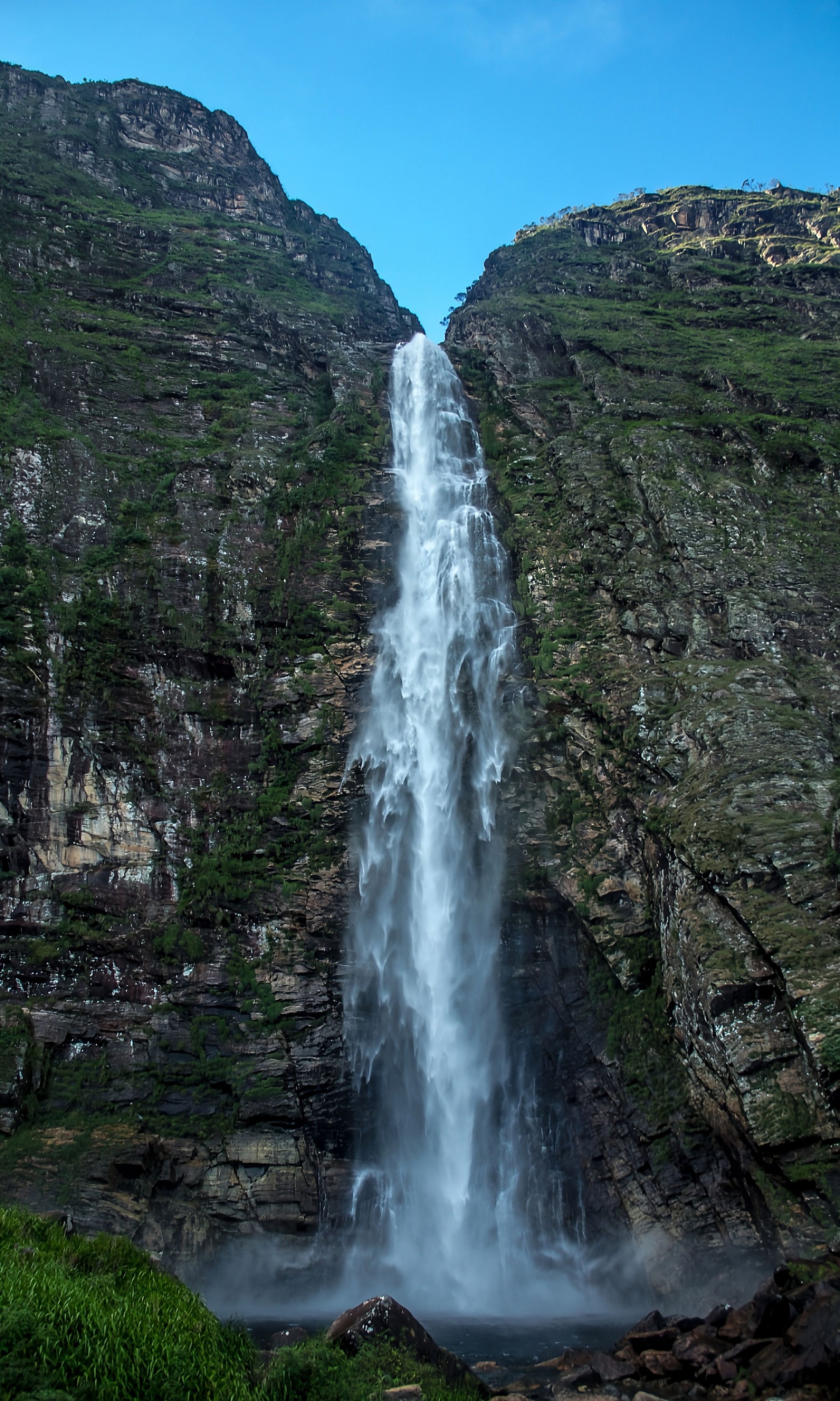 A tall waterfall cascading between rocky green slopes