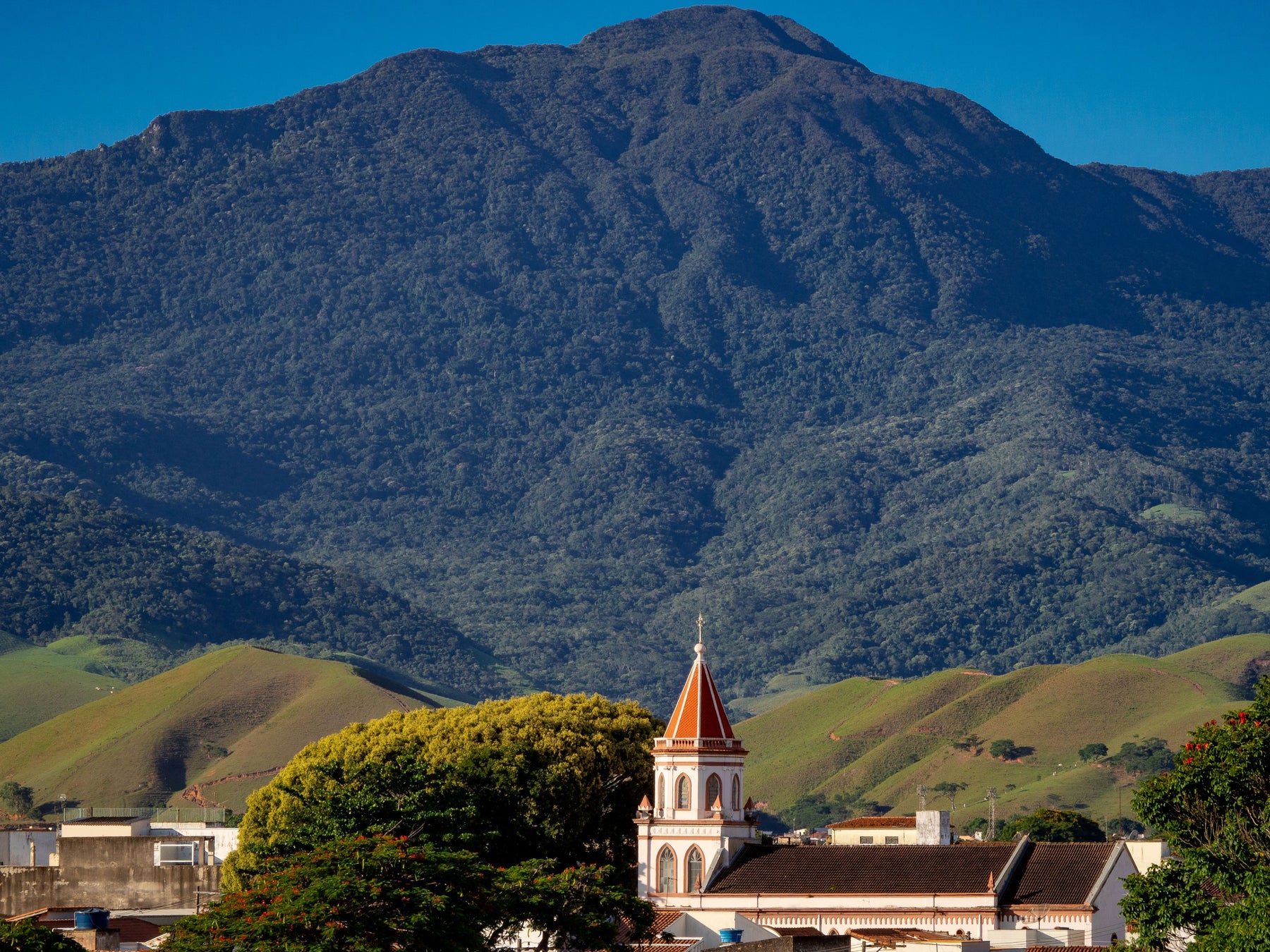 A church and town rooftops beneath a green mountain